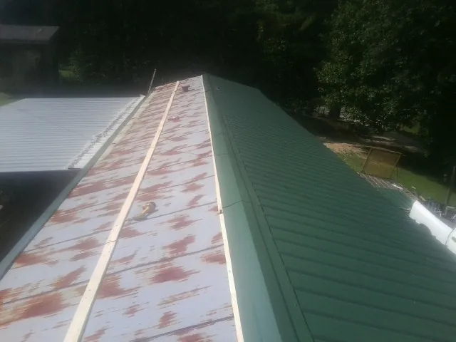 Old rusted panels beside newly installed green metal roofing — Wind Damage Roof Repair by Roofing Brothers in Spray
