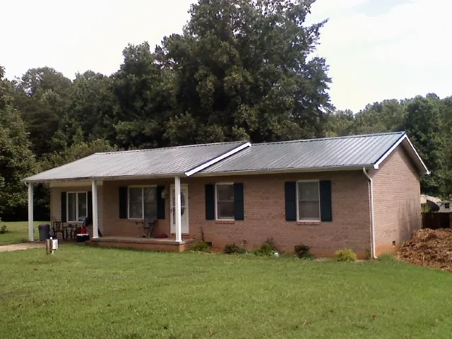 Gray metal roof on a brick ranch house with a side carport in Spray
