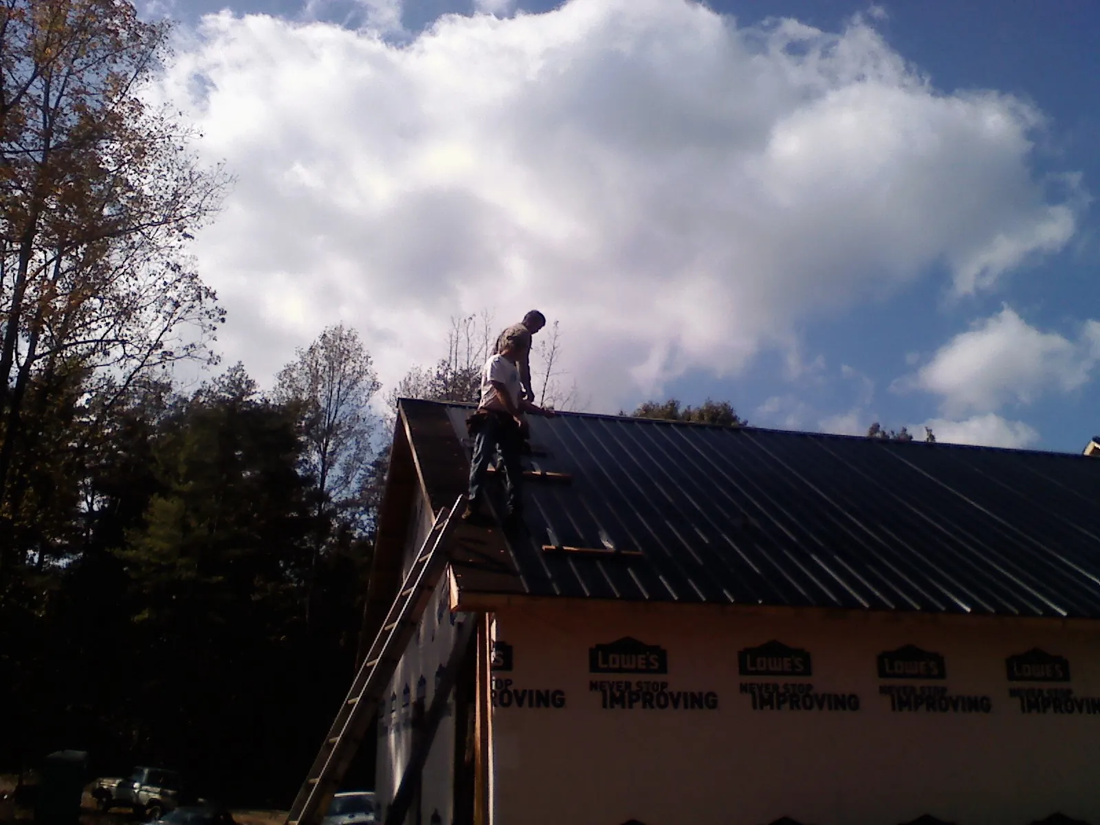 Roofer fastening dark metal panels high against a cloudy sky, from a Roof Inspection job in Spray